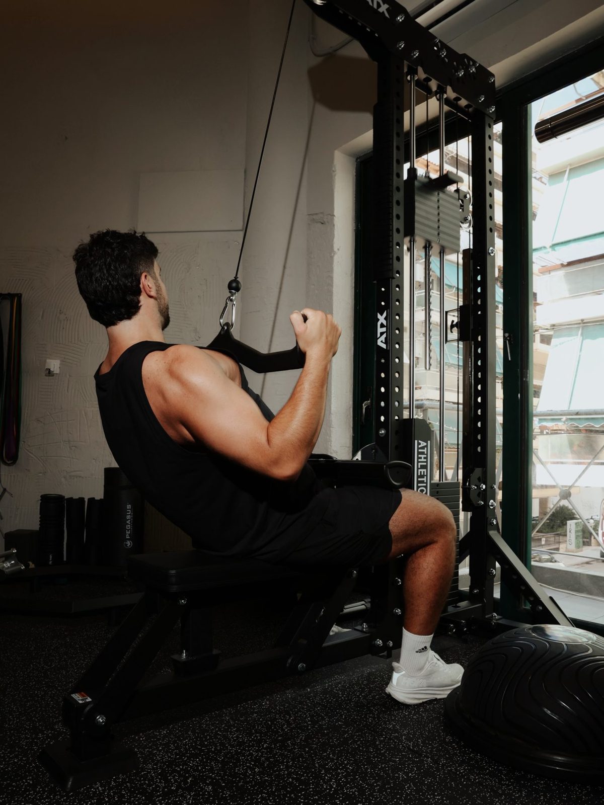 A member training on a cable machine beside a large window