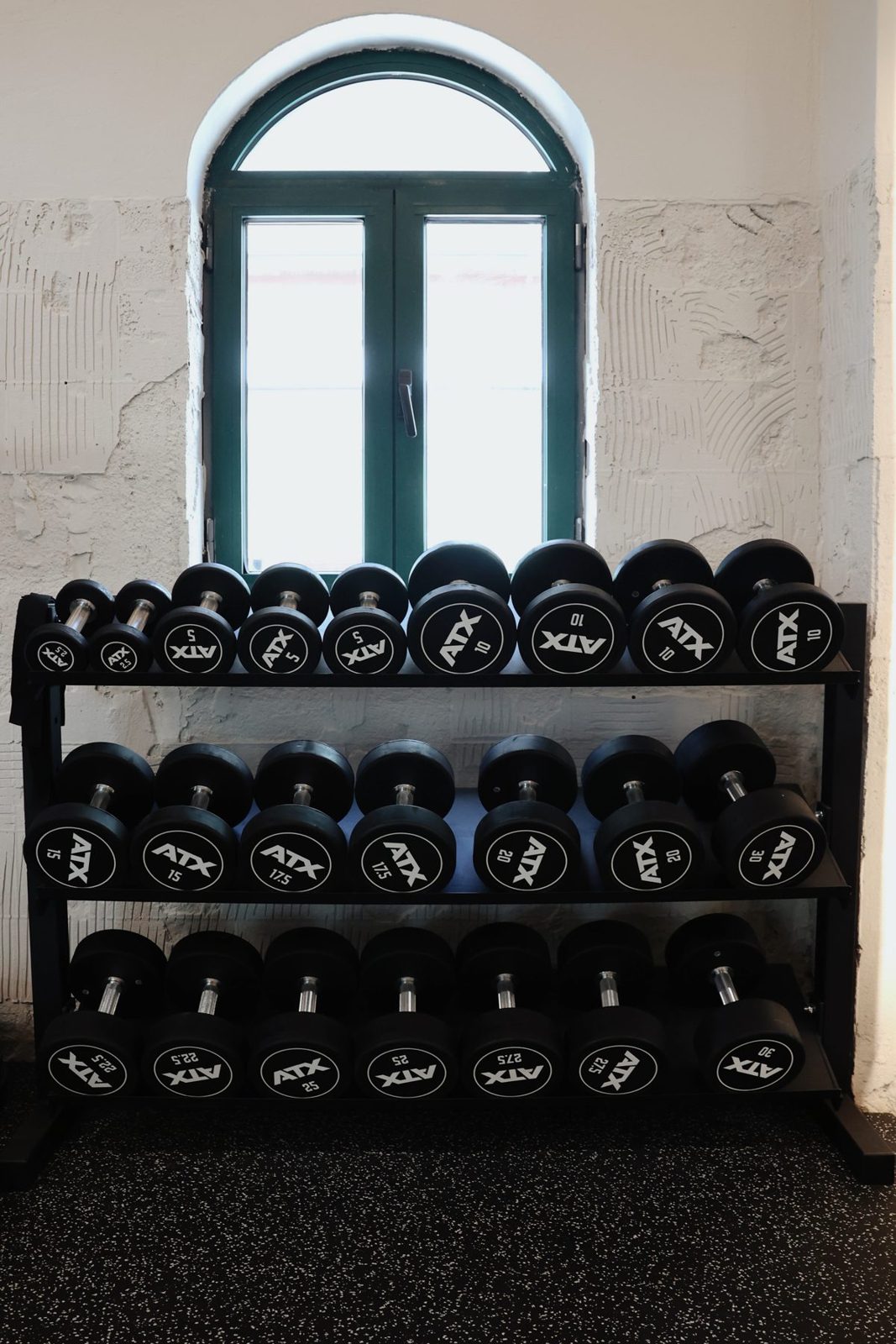Racks of black dumbbells beneath an arched green-framed window