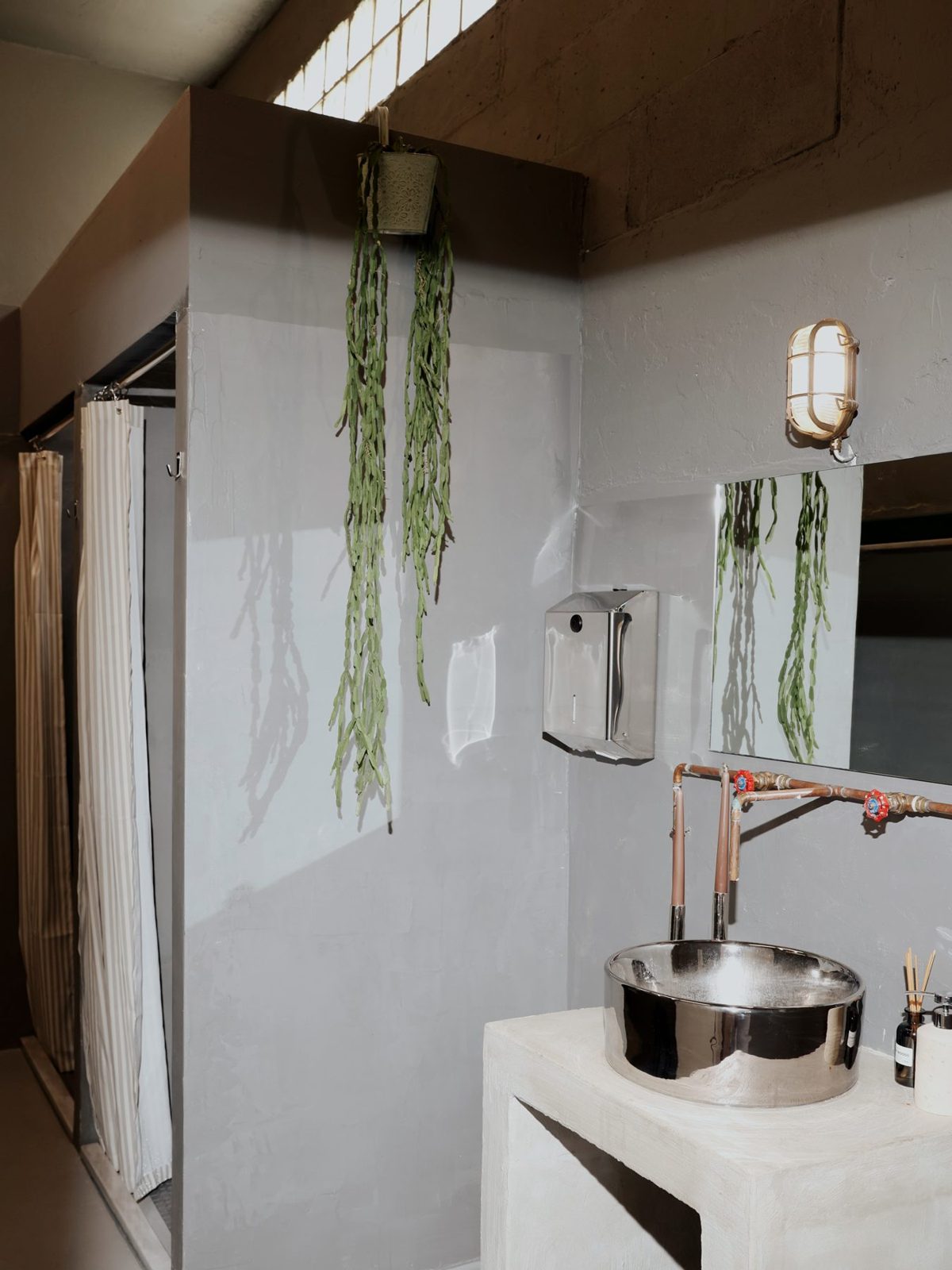 Concrete washbasin with copper pipes and hanging plants beside the showers